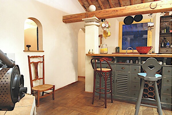 A kitchen with wooden beams, a bar stool, a high chair, and a sink.