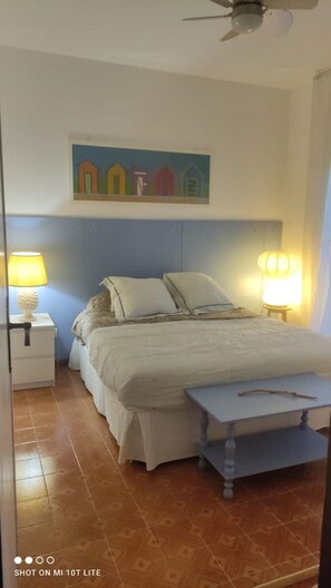 Un dormitorio con cama, dos lámparas de noche, una mesita de noche, una mesita pequeña y un ventilador de techo.