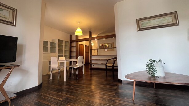 A modern living room with a dark wood floor, white furniture, a television, and a dining area with chairs and a table. - Apartment in the exhibition center, clinic, near the historic center (Arezzo)