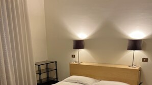 A neatly made bed with white linens and a brown patterned bedspread, two bedside lamps, a small table, and a wooden headboard. - Apartment in the exhibition center, clinic, near the historic center (Arezzo)