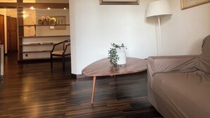 A modern living room with a wooden floor, a beige sofa, a small round table with a plant, a white lamp, and a framed picture on the wall. - Apartment in the exhibition center, clinic, near the historic center (Arezzo)