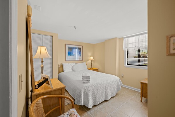 Una habitación de hotel con cama, lámparas de noche, una silla, un escritorio y una ventana con persianas.