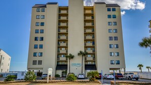 A multi-story hotel with a central atrium, balconies, and a parking area with several vehicles. - Nicely decorated Oceanfront Condo + Free Attraction Tickets! (North Myrtle Beach)
