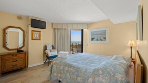 A bedroom with a bed, a dresser, a chair, a TV, and a balcony with a view. - Nicely decorated Oceanfront Condo + Free Attraction Tickets! (North Myrtle Beach)