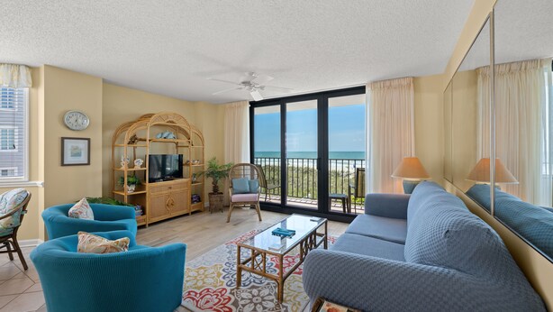 A spacious living room with a large sofa, a coffee table, and a television. There is a balcony with a view of the ocean. - Nicely decorated Oceanfront Condo + Free Attraction Tickets! (North Myrtle Beach)
