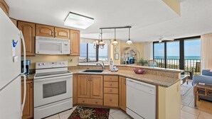 A kitchen with wooden cabinets, a white stove, and a large island with a sink. - Nicely decorated Oceanfront Condo + Free Attraction Tickets! (North Myrtle Beach)