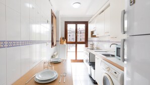 A modern kitchen with white cabinets, a wooden countertop, a washing machine, and a view through a glass door. - Eihera - baskeyrentals (Irun)