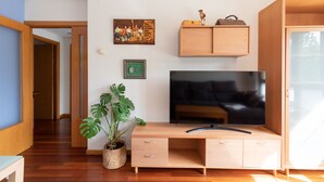 A living room with a wooden TV stand, a large flat-screen TV, a potted plant, a framed picture, and a wooden cabinet. - Eihera - baskeyrentals (Irun)