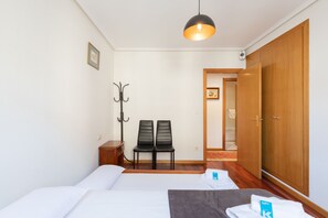 A bedroom with a bed, two chairs, a coat rack, a wooden wardrobe, and a hanging light fixture. - Eihera - baskeyrentals (Irun)