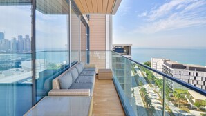 Ein moderner Balkon mit Glasgeländer, einem grauen Sofa und Holzboden.