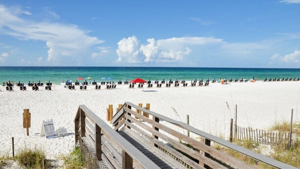 A beach with a wooden boardwalk leading to the shore, rows of beach chairs, and umbrellas. - Leah’s Sunset Dreams Studio (Miramar Beach)