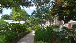 A pathway lined with lush greenery and palm trees, leading to a row of buildings with balconies. - Leah’s Sunset Dreams Studio (Miramar Beach)