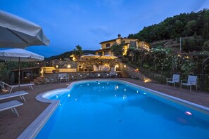 Une piscine entourée d’un mur de pierre et bordée d’une colline, avec des chaises longues et des parasols.