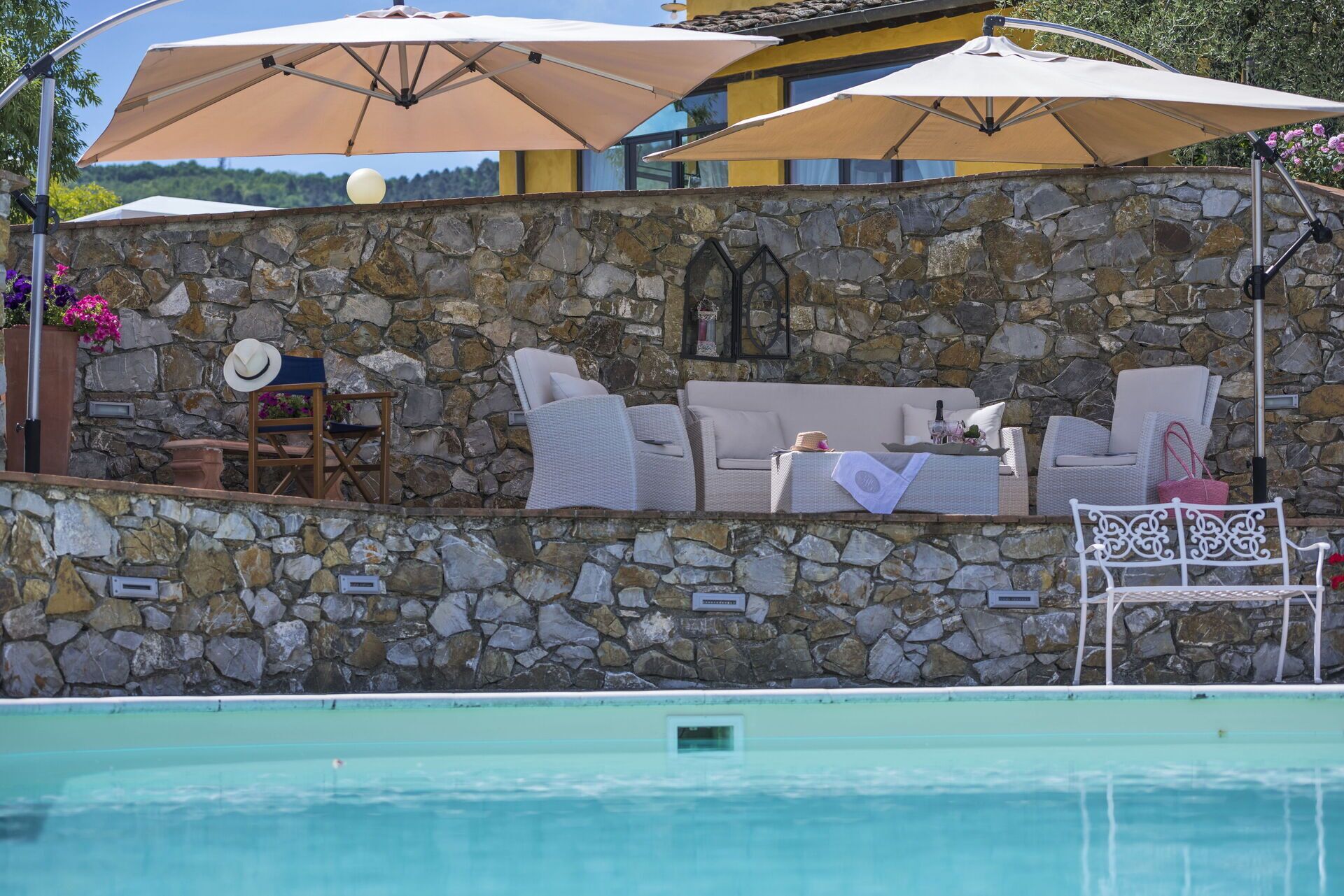 A stone wall with outdoor seating, a pool, and umbrellas.
