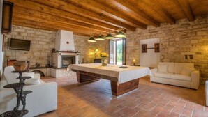 Ein rustikales Interieur mit freiliegenden Holzbalken, einem Steinkamin, einem zentralen Inseltisch und einem weißen Sofa.