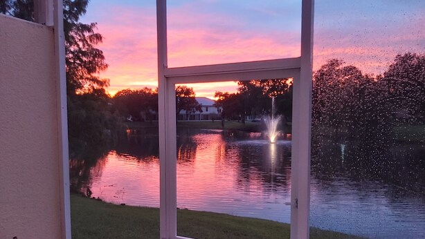 A view of a lake at sunset through a window, with a fountain in the center. - Smart home near Disney World, Universal Studios, Silver Spurs Arena (Kissimmee)