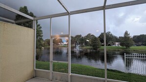 A view through a glass enclosure overlooking a pond with a fountain, surrounded by greenery and residential buildings. - Smart home near Disney World, Universal Studios, Silver Spurs Arena (Kissimmee)
