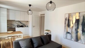 Ein modernes Wohnzimmer mit einem dunklen Sofa, einem Esstisch und einer Küche im Hintergrund.