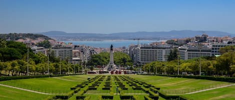 A large, open public space with a central monument, surrounded by neatly trimmed hedges and a variety of buildings in the background.