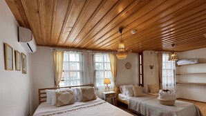 A room with two beds, wooden ceiling, large windows with curtains, a hanging light fixture, and a small table with a lamp. - Hanole Guest House (Ayvalik)