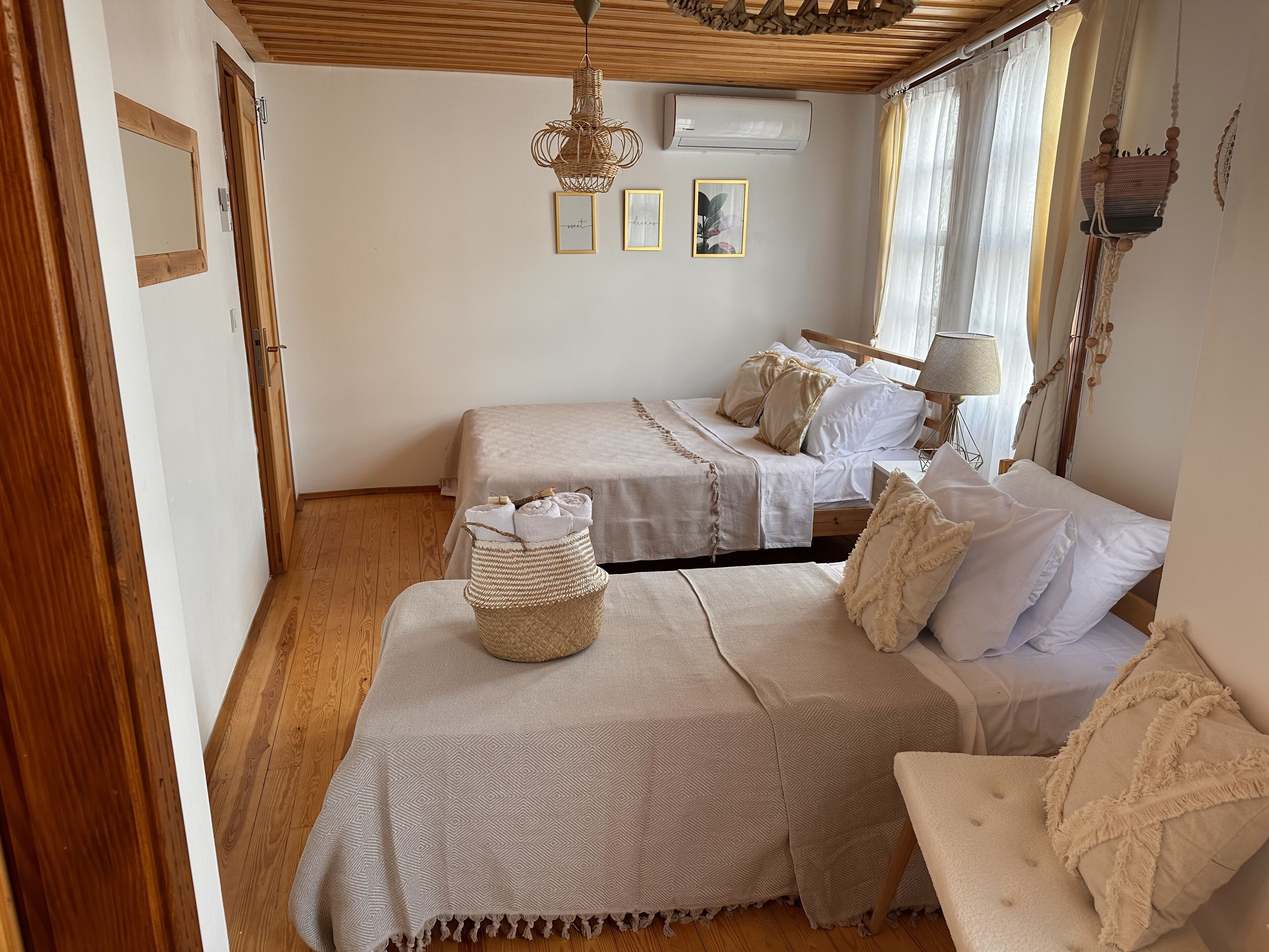 Ein Schlafzimmer mit zwei Betten, Holzboden, einer Pendelleuchte und einem Fenster mit Vorhängen.