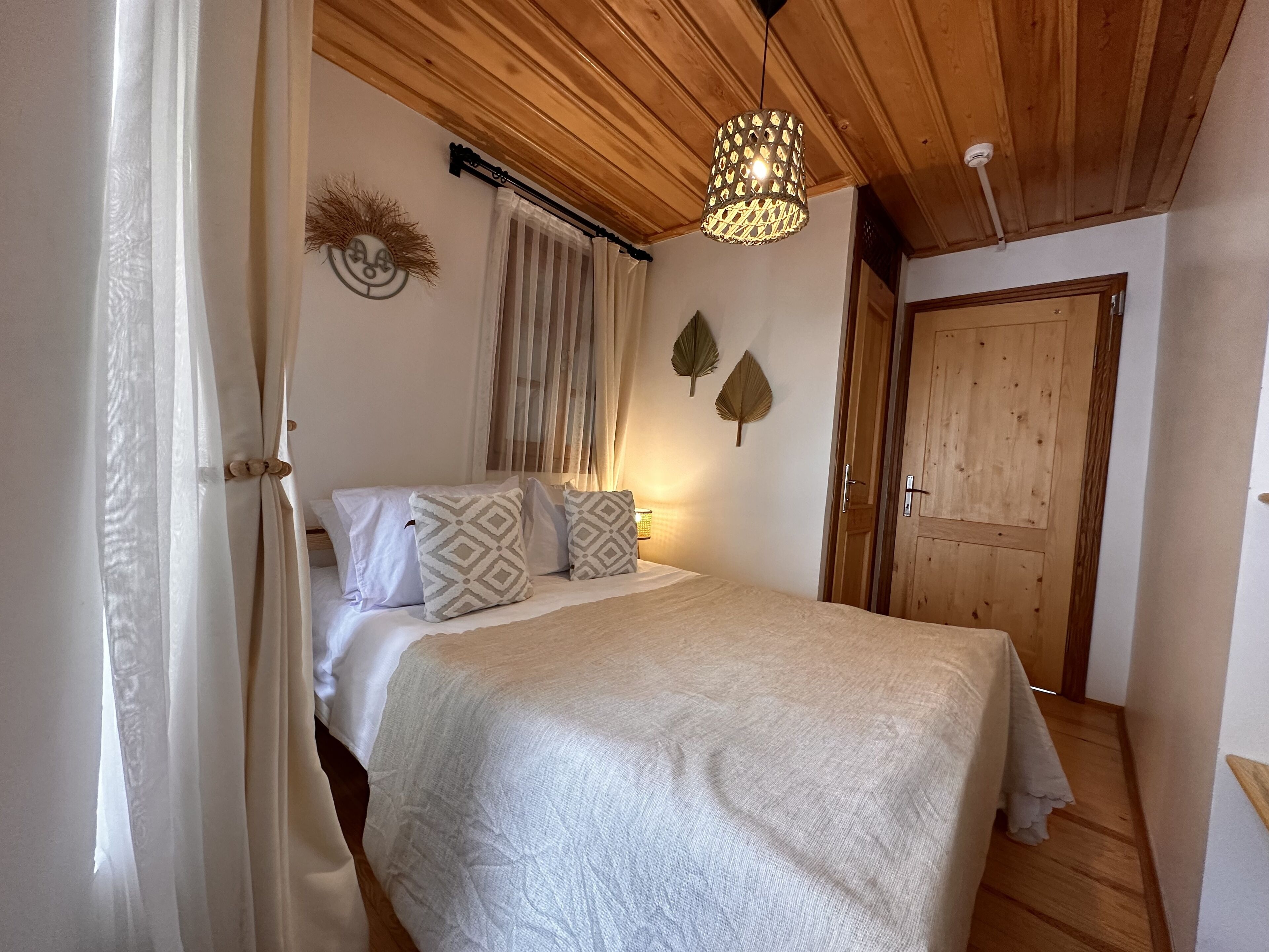 A bedroom with a bed, a hanging light fixture, a wooden door, and a window with curtains.