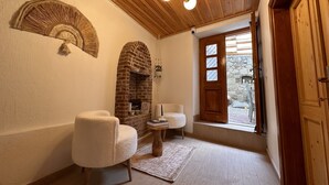 A cozy room with a brick fireplace, two plush chairs, a small table, and a wooden ceiling with a chandelier. - Hanole Guest House (Ayvalik)
