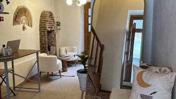 A cozy living room with a wooden ceiling, a brick fireplace, a dining area with a table and chairs, and a staircase leading to another level.