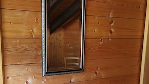 A wooden cabin interior with a wooden desk, a mirror, a potted plant, and a trash bin. - Pension Lärch (Obergoms)