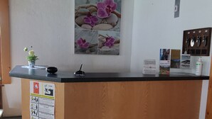 A reception desk with a wooden finish, a wall-mounted calendar, and a framed picture of flowers. - Pension Lärch (Obergoms)