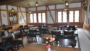 A restaurant with wooden beams, large windows, and a variety of seating arrangements including tables and booths. - Pension Lärch (Obergoms)