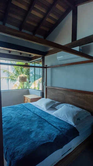 A room with a bed, a window with a view of palm trees, and a hanging light fixture. - Casa pé na areia com piscina | São Sebastião (São Sebastião)