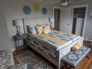 A bedroom with a bed, bedside tables, a bench, a wardrobe, and decorative wall pieces. - Quiet family escape and just 5min drive to the beaches. (Middletown)