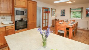A modern kitchen with wooden cabinets, a built-in microwave, oven, and a dining area with a table set for two. - Byewater (Ryde)