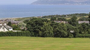 A coastal view with houses, a grassy field, and a mountain in the distance. - Haddef Penmaenmawr (Penmaenmawr)