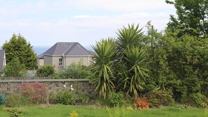 A residential area with a house, a stone wall, and various plants. - Haddef Penmaenmawr (Penmaenmawr)