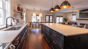 A modern kitchen with a large island, pendant lighting, and wooden flooring.
