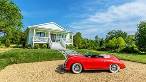 A light blue house with a white porch and a red convertible parked in front.