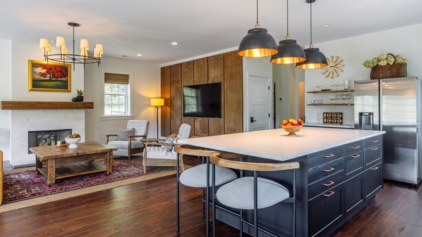 A modern kitchen with a large island, pendant lighting, and a flat-screen TV.