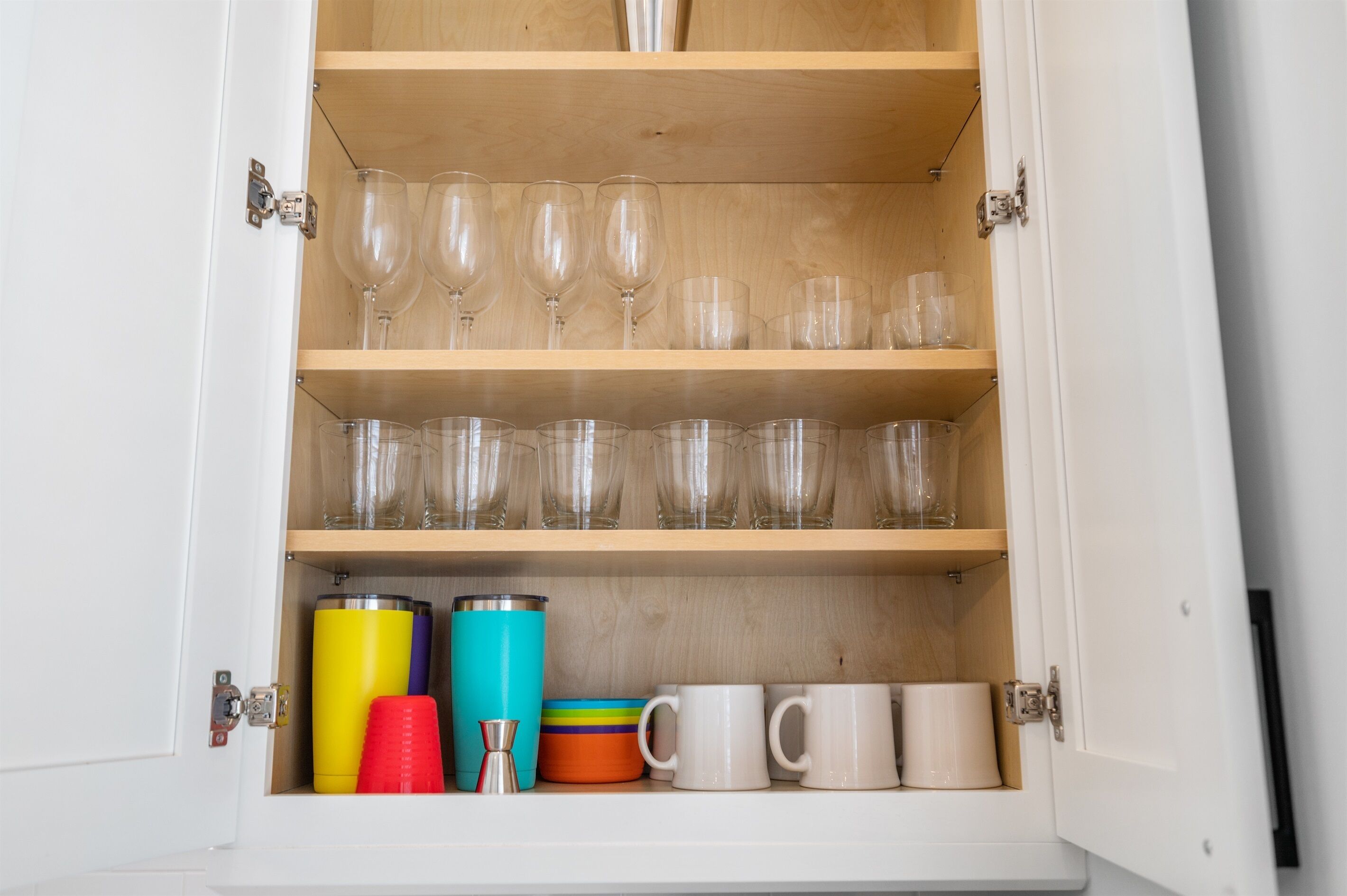 A cabinet with shelves containing wine glasses, tumblers, and mugs.