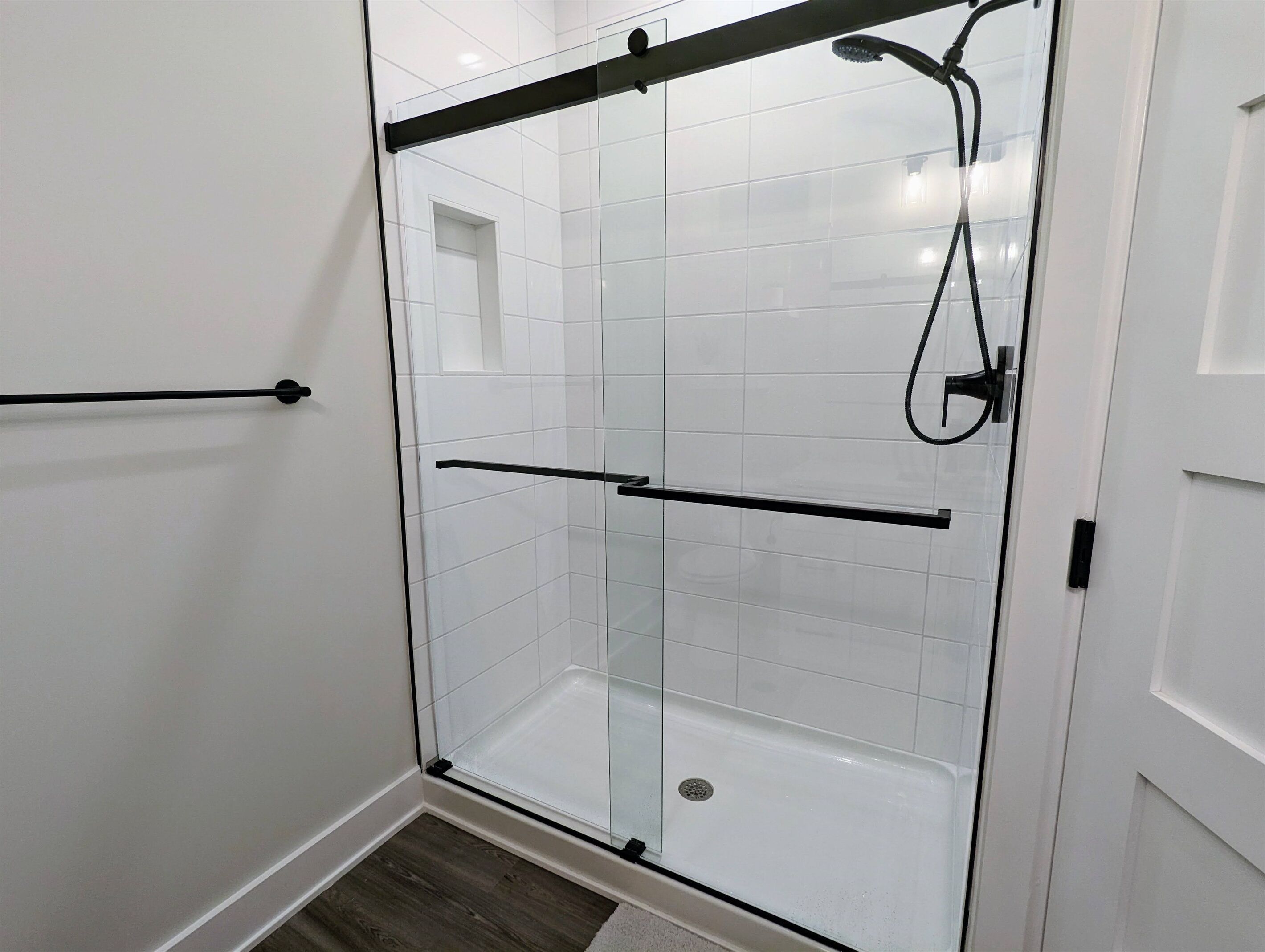 A glass-enclosed shower stall with a black towel bar and a handheld showerhead.