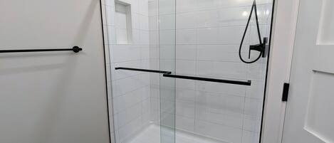 A glass-enclosed shower stall with a black towel bar and a handheld showerhead.