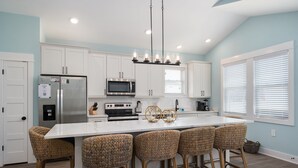 Una cocina moderna con armarios blancos, un refrigerador de acero inoxidable, un microondas y una isla grande con taburetes de bar.