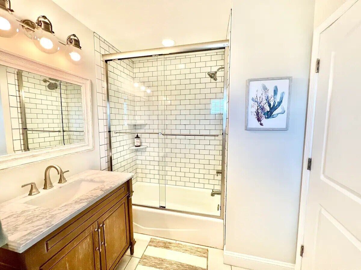 A bathroom with a white-tiled shower, a large mirror, and a vanity with a marble countertop.
