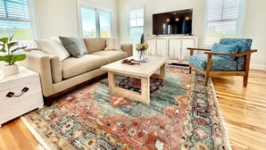 Een woonkamer met een beige bank, een houten salontafel, een blauwe fauteuil en een televisie op een witte kast.