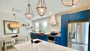 Een moderne keuken met blauwe kastjes, een groot kookeiland, roestvrijstalen apparatuur en hanglampen.