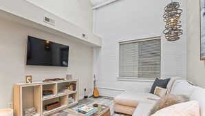A modern living room with a flat-screen TV, a bookshelf, a sofa, and a hanging light fixture. - Chic Downtown Loft - Parking - Central New (Wilmington)