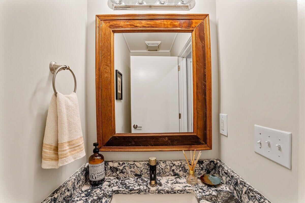 A bathroom with a marble sink, a wooden-framed mirror, a towel rack, and a bottle of hand soap.