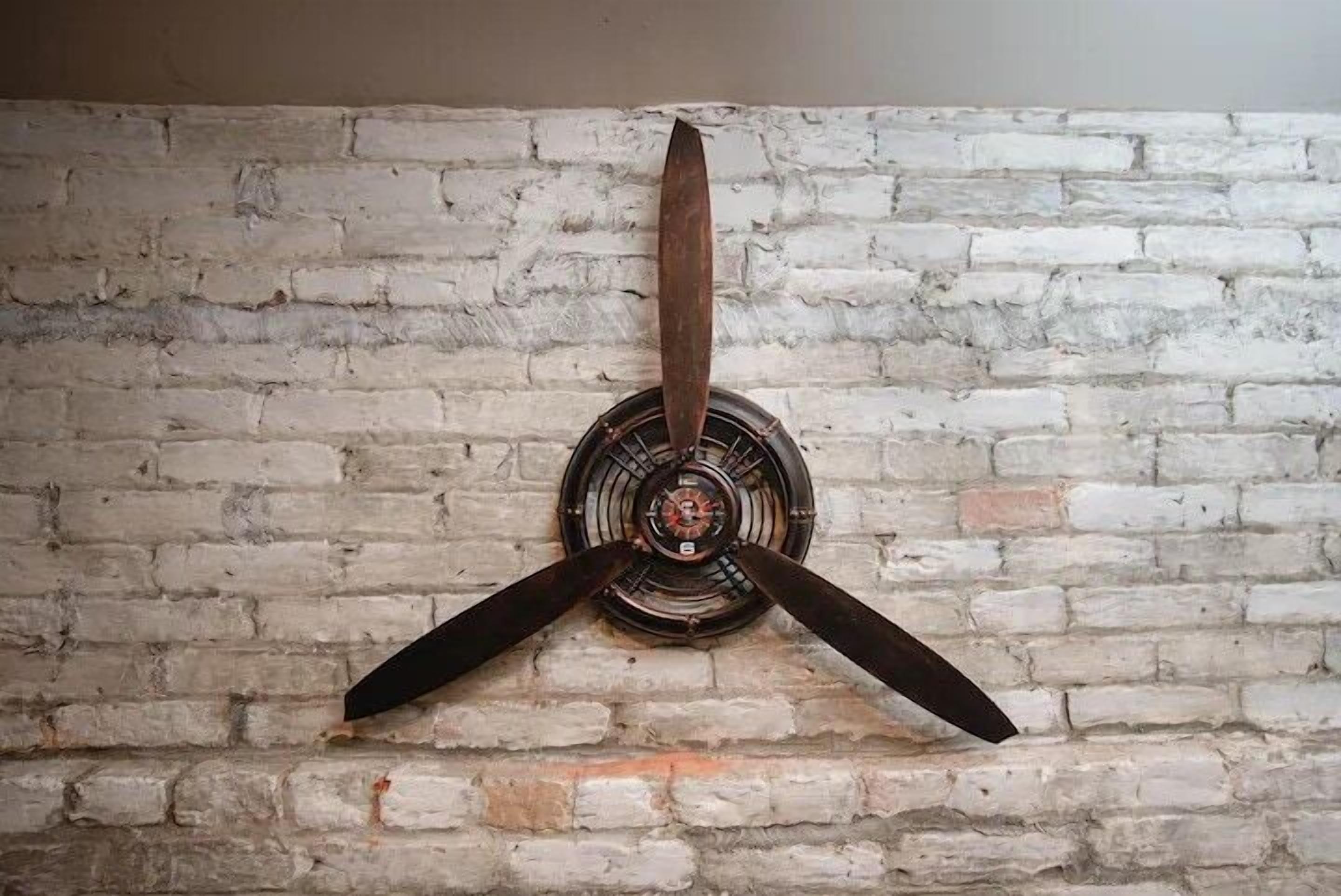 Un ventilateur de plafond fixé au mur, doté de trois pales et d’un luminaire central, installé devant un mur en briques.