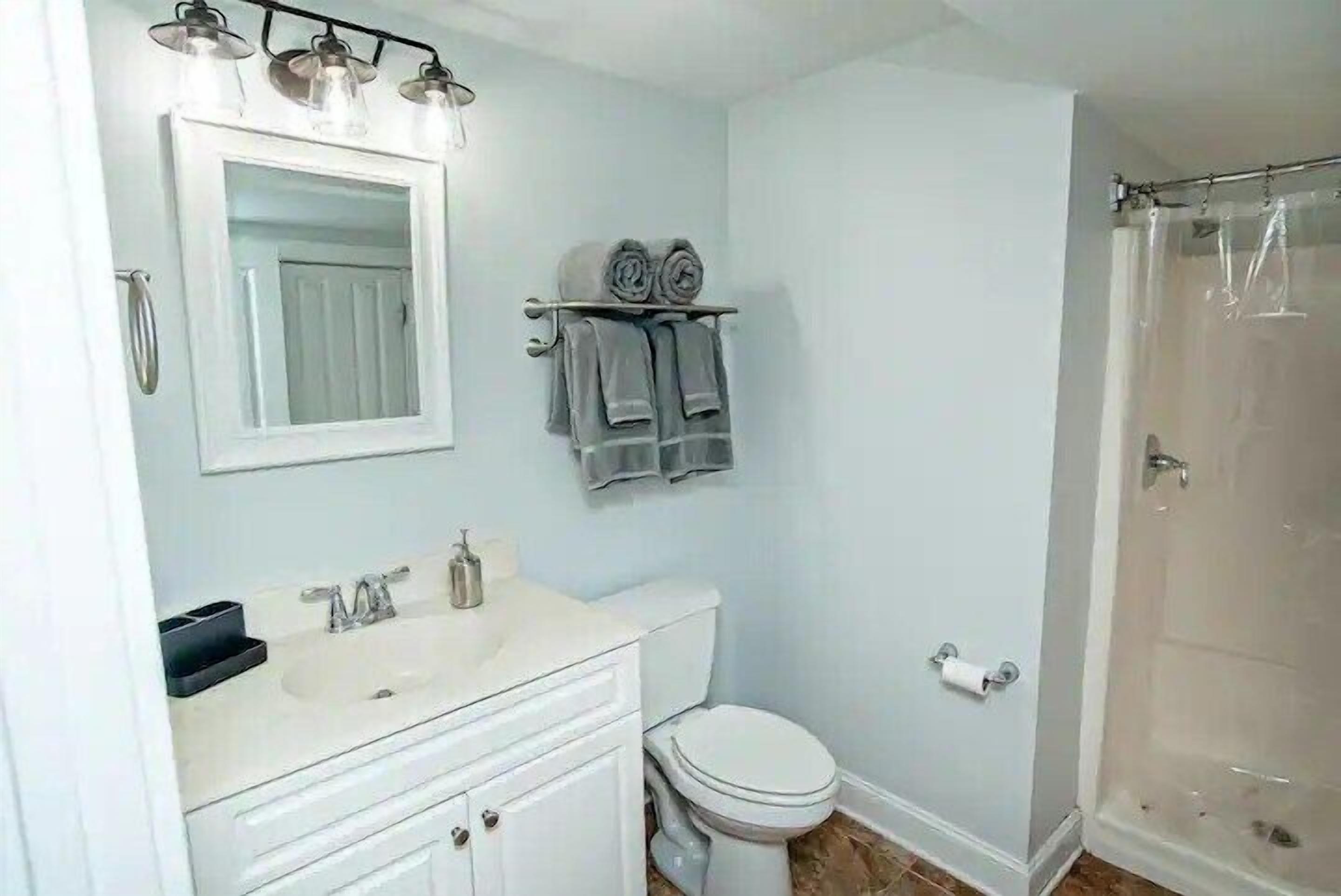 A bathroom with a white sink, mirror, and toilet. There are towels on a rack and a shower curtain.